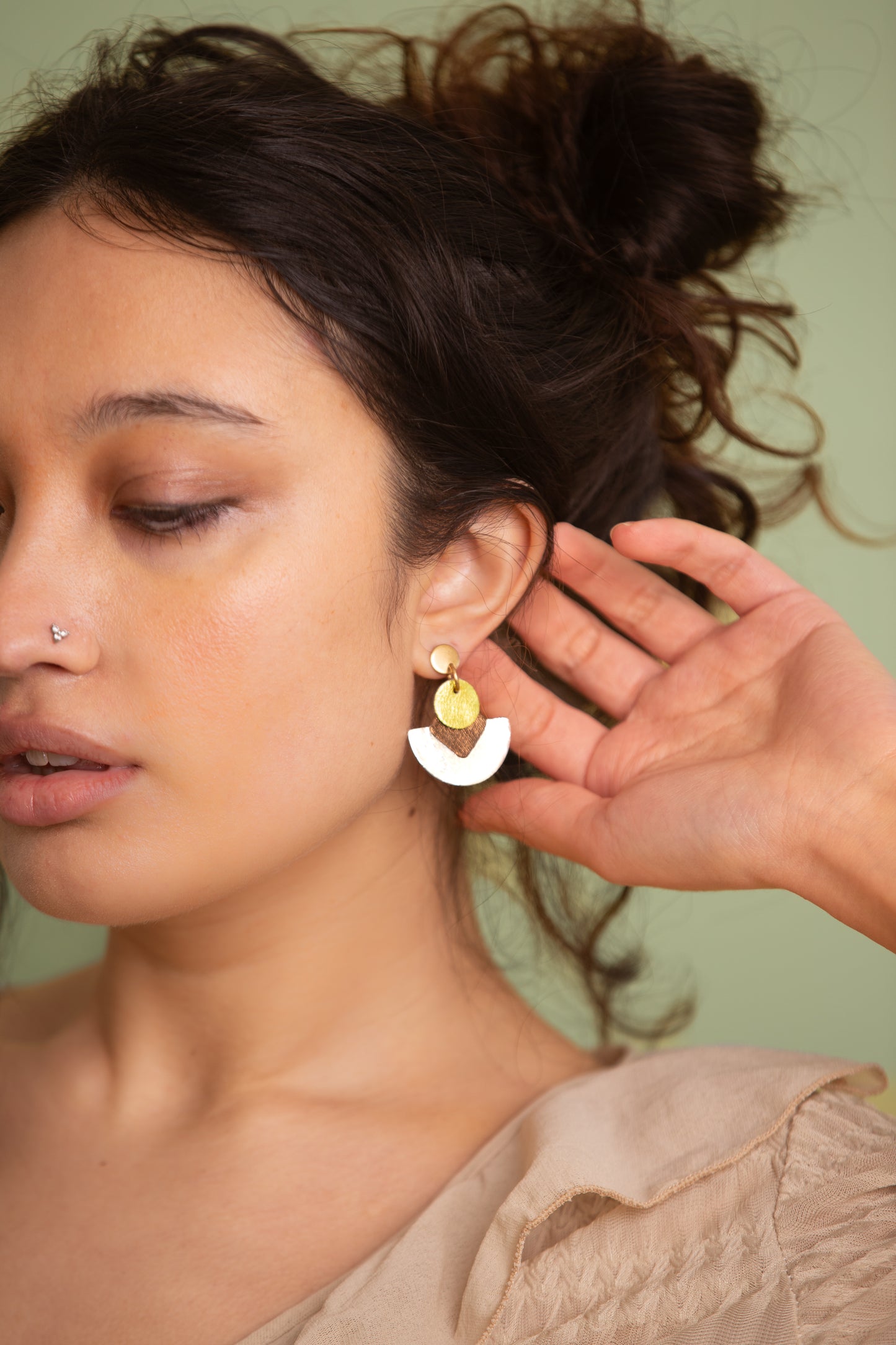 Close-up of a woman wearing a gold earring with a green background