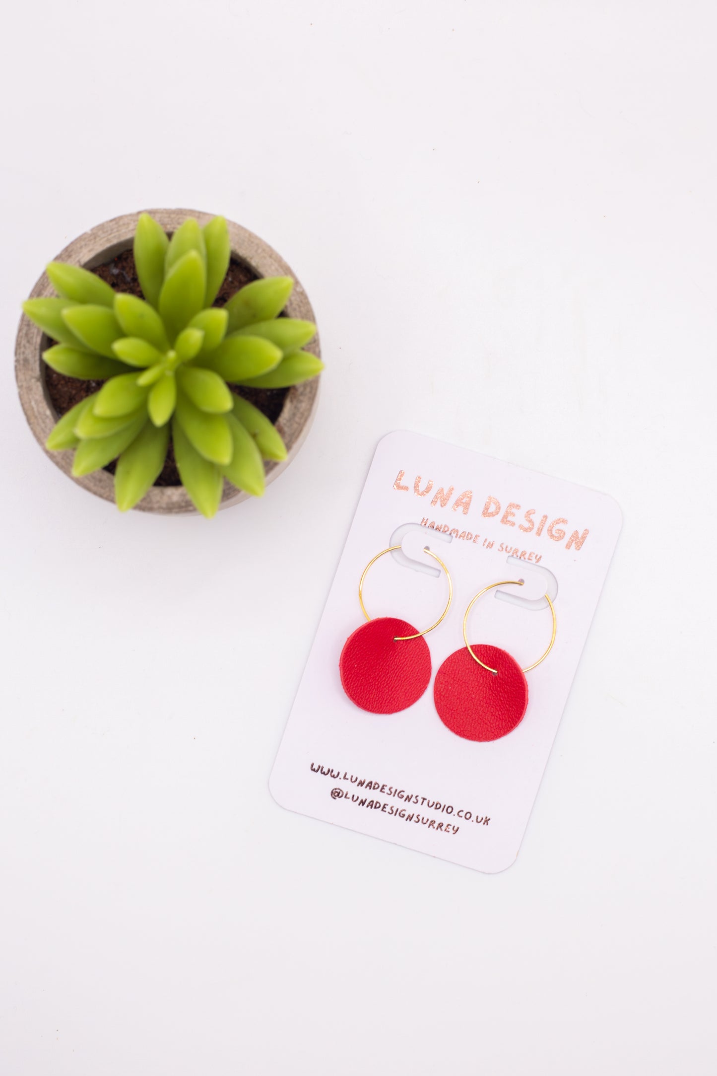 Red earrings on a Luna Design card with a small plant on a white background