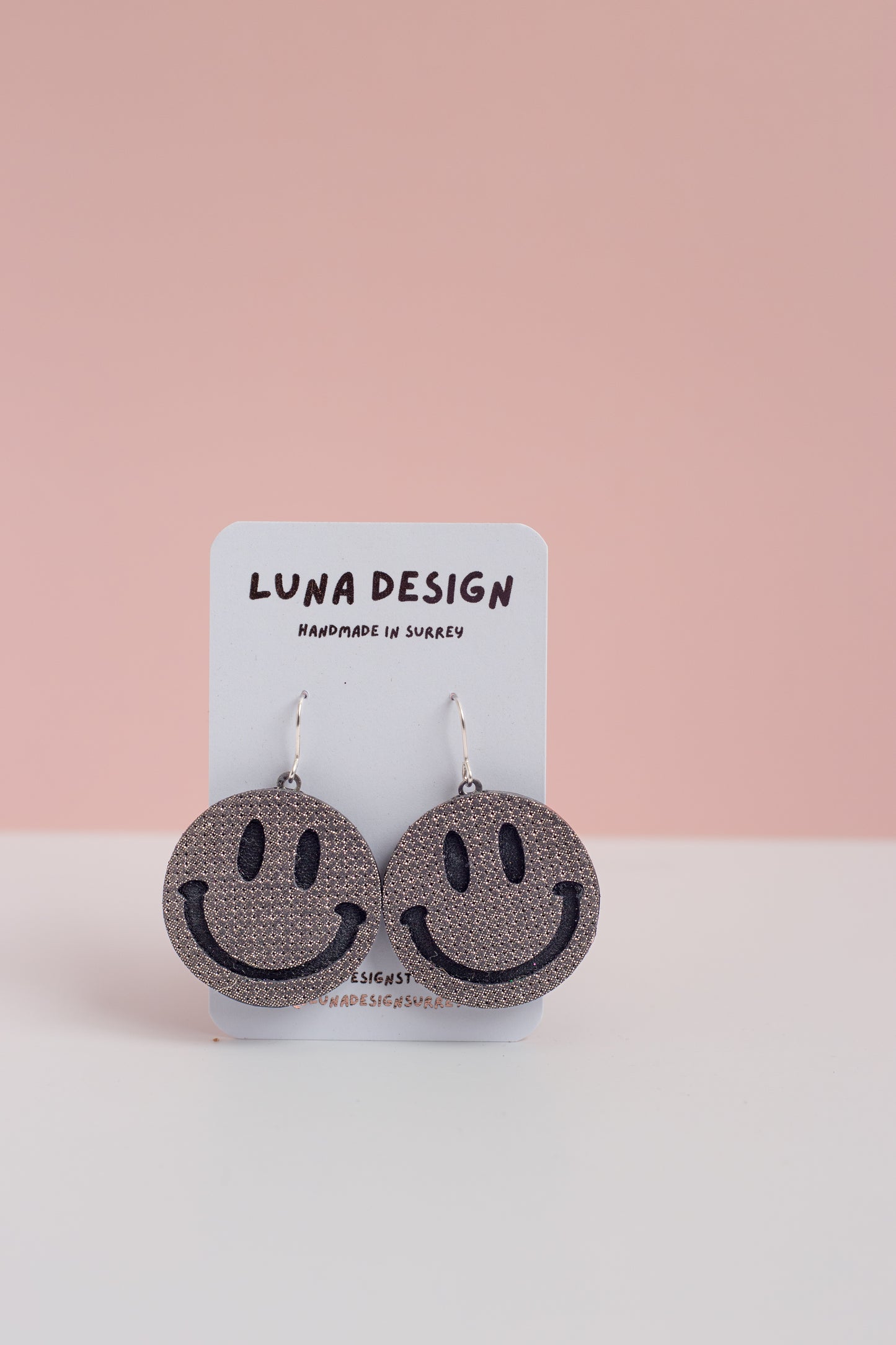 Smiley face earrings on a Luna Design card with a pink background