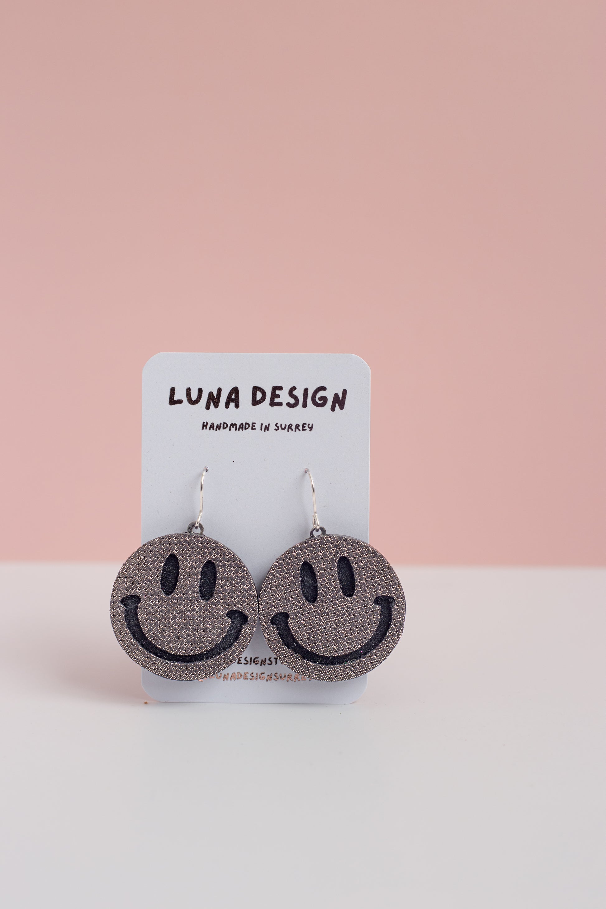 Smiley face earrings on a Luna Design card with a pink background
