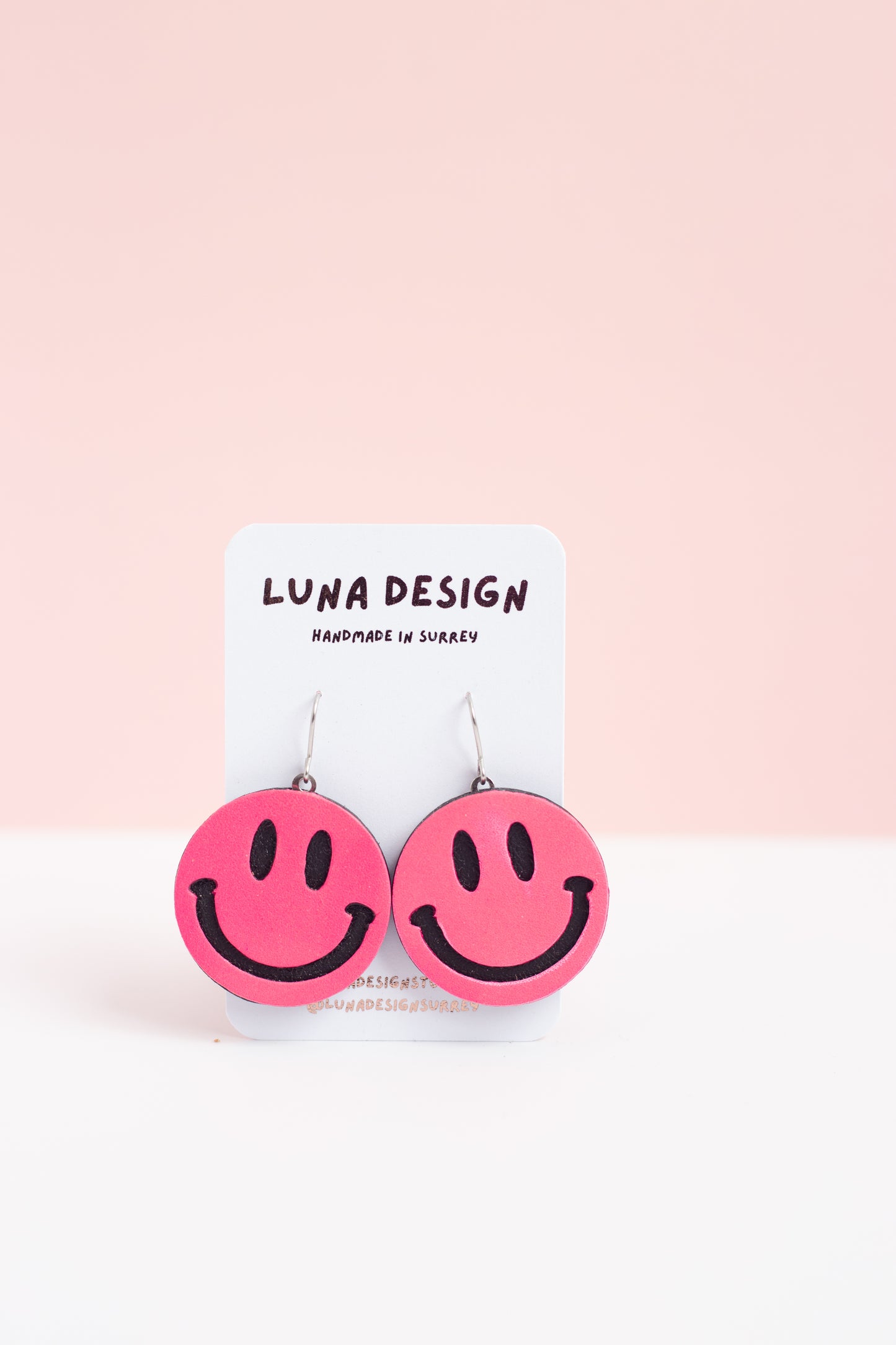 Pink smiley face earrings on a Luna Design card against a pink background