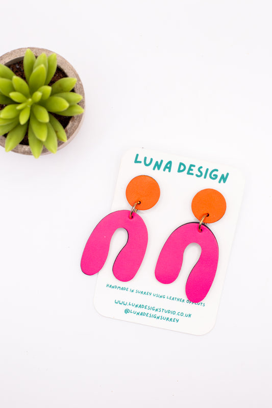 Pink U-shaped earrings with orange circular pads on a white background with 'Luna Design' branding.