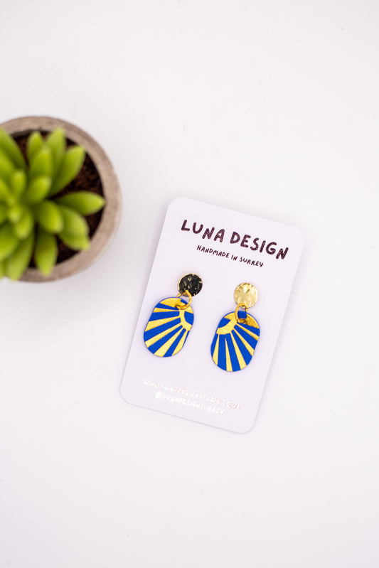 Blue and gold earrings on a Luna Design card with a plant in the background