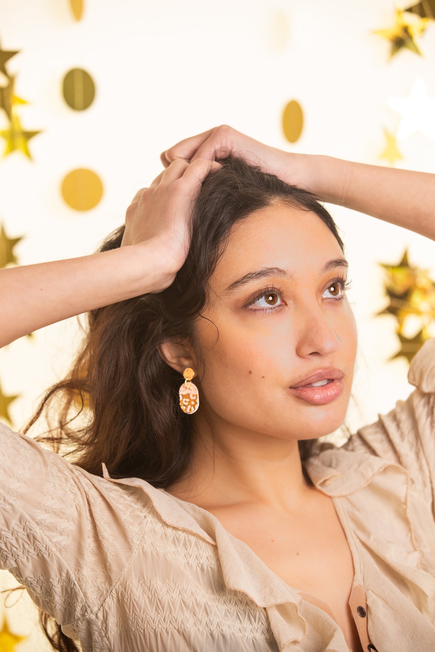 Woman with hands in hair against a gold polka dot background