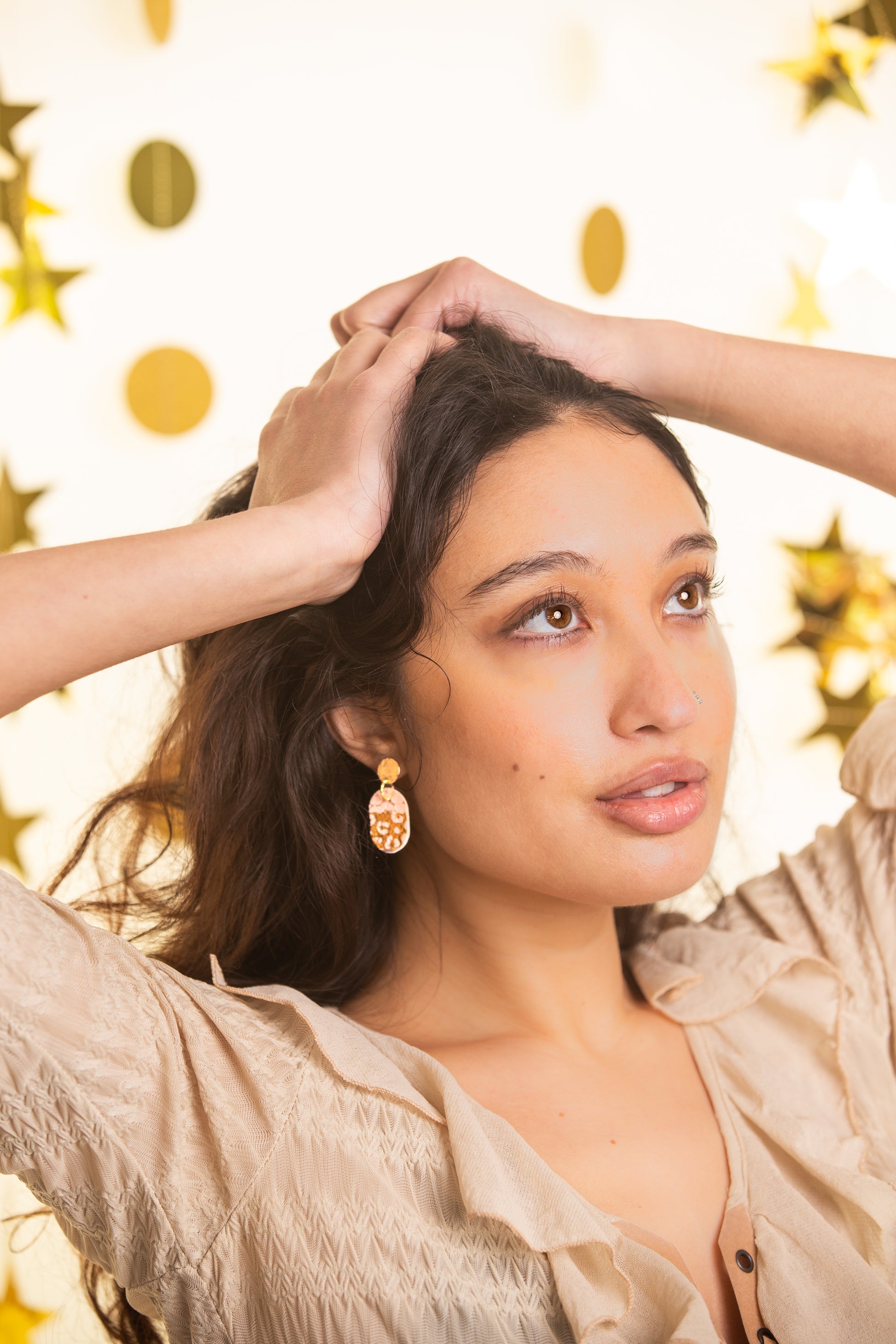 Woman with hands in hair against a gold polka dot background