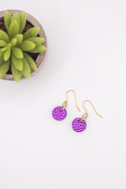 Purple earrings on a white surface with a small potted plant in the background