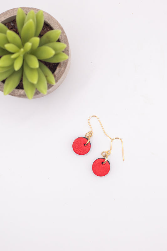 Red earrings on a white surface with a small plant in the background