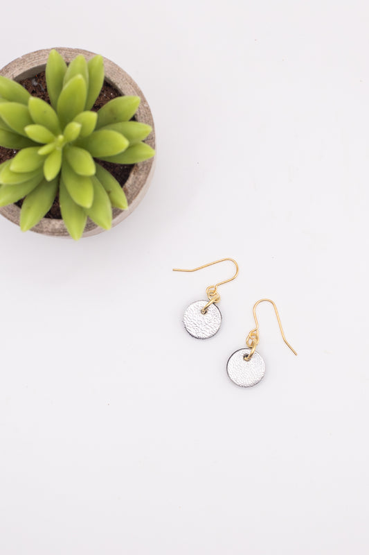 Gold and silver earrings on a white surface with a small potted plant.