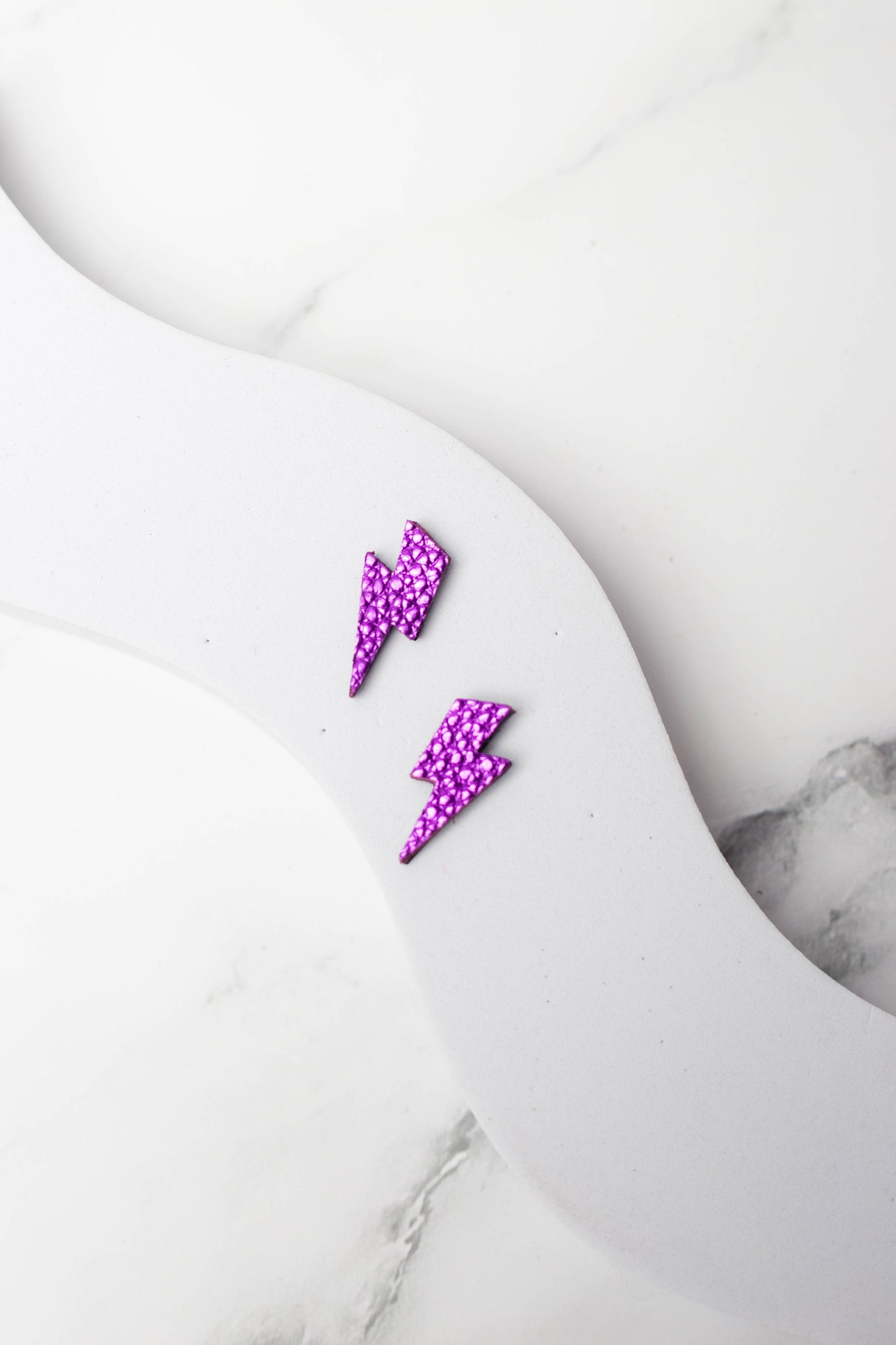 Purple lightning bolt earrings on a marble surface
