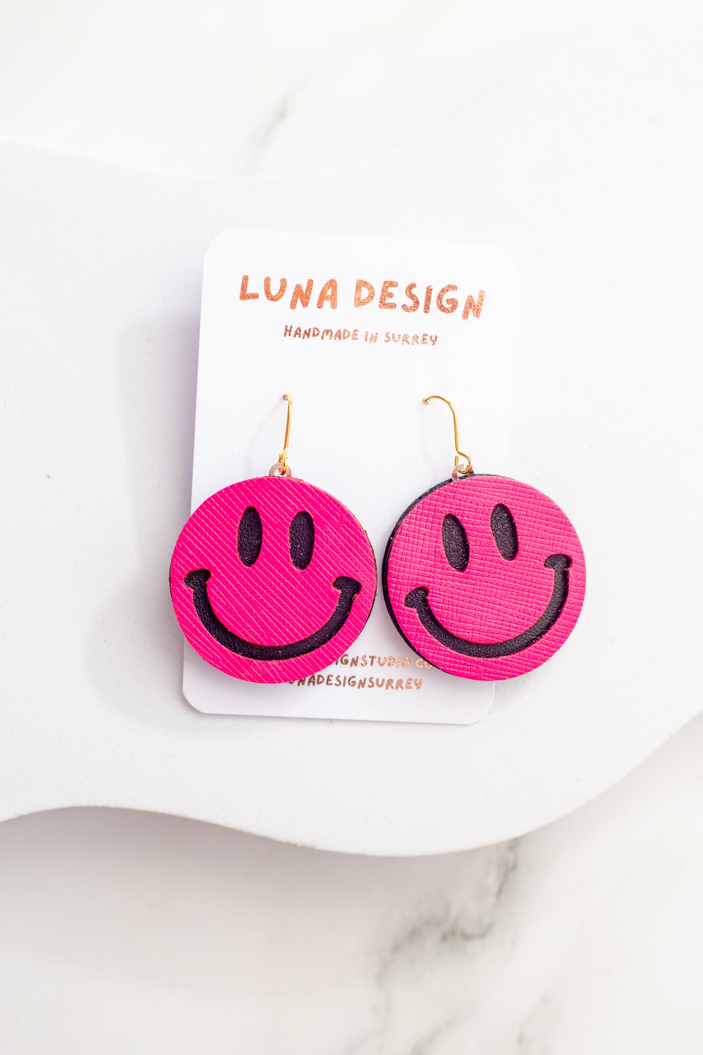 Pink smiley face earrings on a white card with 'LUNA DESIGN' branding.